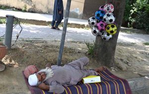 An elderly vendor enjoys a nap at roadside setup while selling balls at Peshawar Morr
