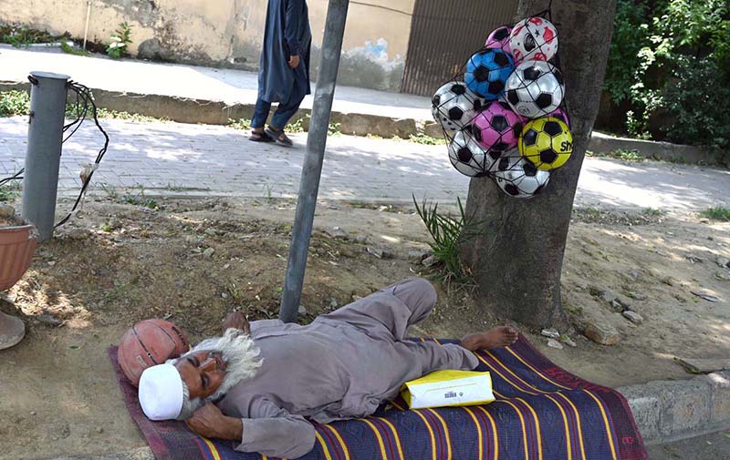 An elderly vendor enjoys a nap at roadside setup while selling balls at Peshawar Morr