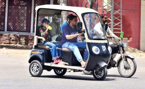 A woman and a child traveling in an electric tri-cycle rickshaw at Court Road.