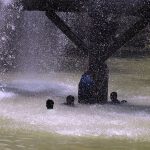A youngster enjoys bathing in water leaking from a supply line at Channel Mori Canal during hot weather