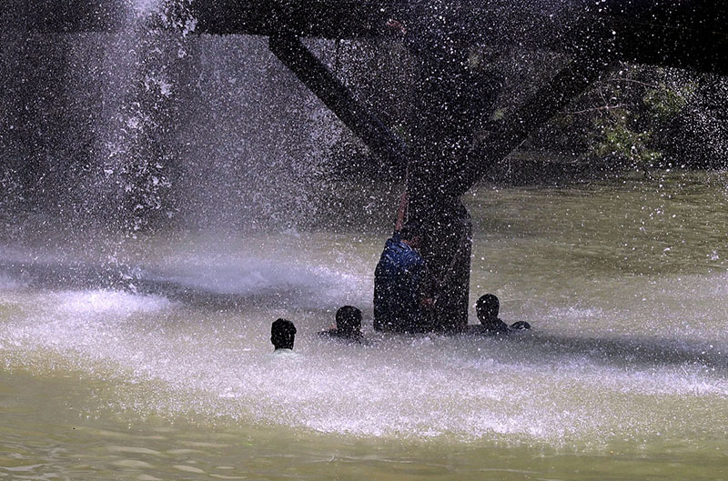 A youngster enjoys bathing in water leaking from a supply line at Channel Mori Canal during hot weather