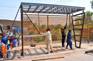 Workers are busy installing a steel-framed roadside bus stop along a city road as part of ongoing infrastructure and public facility improvement works.