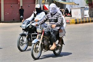 Motorcyclists cover their faces with a cloth to protect from the scorching sun and heatwave conditions as soaring temperatures continue to grip the city.