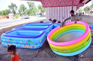 A vendor displays inflatable swimming pools under a flyover in Qasimabad, hoping to attract customers seeking relief from the sweltering summer heat.