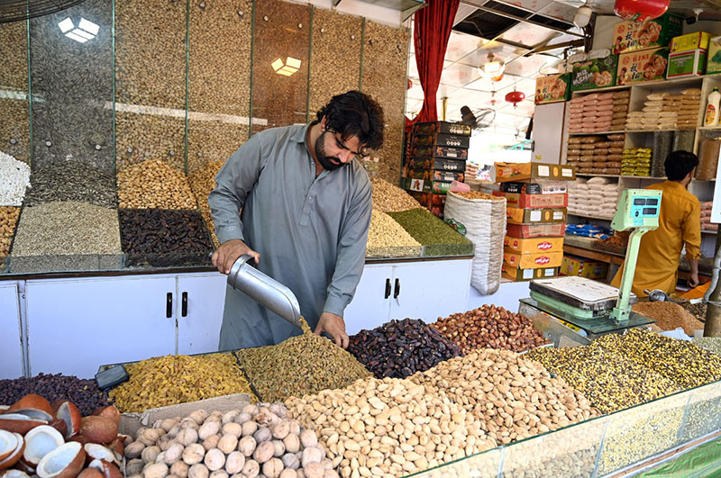 A vendor arranges a variety of dry fruits, including dates, raisins and nuts, on display at his shop weekly bazaar at Peshawar Mor, H-9 in the Federal Capital