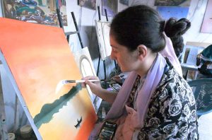 A young female artist puts the finishing touches on a vibrant oil painting, The canvas depicts a stunning sunset landscape with a crescent moon at an art studio training stall in a weekly bazaar in the federal capital.