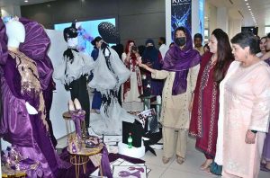 Government College Women University Faisalabad (GCWUF) Vice Chancellor Prof. Dr. Kanwal Ameen examines dresses designed by students during a visit to the 6th Fashion Design Thesis Display at Lyallpur Galleria, showcasing innovative designs, artistic expression, and the creativity of emerging fashion designers.