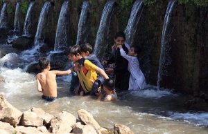 Children play and bathe in a stream at Inqilab Road, Musazai area, to seek relief from the intense summer heat.