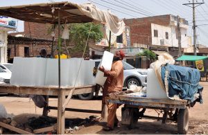 A laborer unloads large ice blocks from a tricycle loader at a roadside vendor stall as demand for ice increases amid scorching summer temperatures in the city