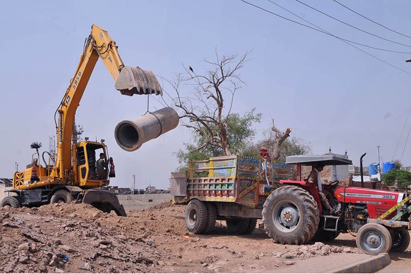 Workers use heavy machinery to load a concrete sewer pipe onto a tractor trolley during ongoing sewerage development work aimed at improving drainage infrastructure in the city