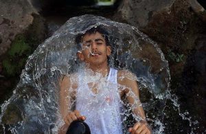 Children play and bathe in a stream at Inqilab Road, Musazai area, to seek relief from the intense summer heat.