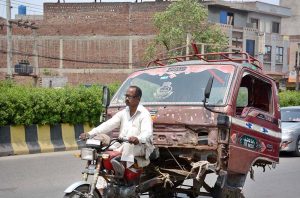 A motorcycle loader rickshaw carries the damaged front portion of a truck to a workshop for repair work in the city.
