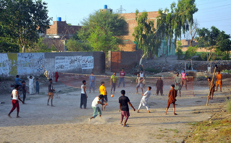 A group of youngsters playing a friendly volleyball match at an open ground in a village area