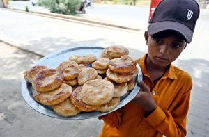 A young street hawker carrying a tray of bakery item Puff pastry on his shoulder for selling at Royal Road in the city.