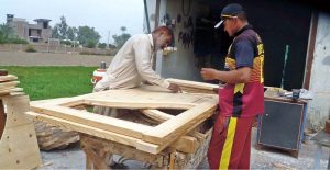Carpenters are busy crafting a wooden door at a roadside workshop, to earning their livelihood.