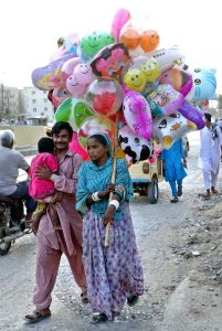 A gypsy family, along with children, walks along a street carrying air-filled toy-shaped balloons for sale to earn a livelihood on a roadside in the city.