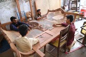 Skilled craftsmen weave intricate cane webbing on elaborately carved wooden furniture at a traditional workshop, keeping alive the centuries-old craft of cane furniture making that provides livelihoods to hundreds of artisans across Country.