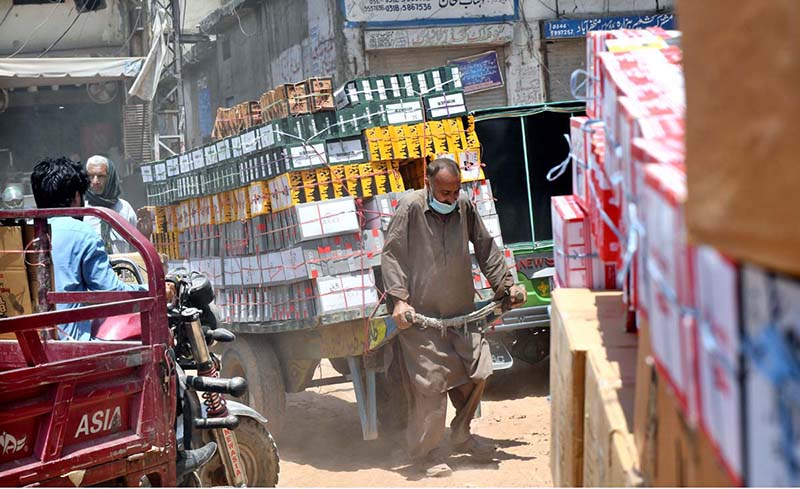 A laborer pulls a heavily loaded handcart through a busy market street, as daily wage workers continue to play a vital role in the city's local trade and transport