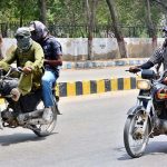 A motorcyclists on the way cover their face with piece of cloth to protect from direct sunlight during hot weather in the city