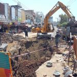 An excavator loads excavated soil onto a tractor trolley during ongoing sewerage and road rehabilitation work on Hussain Agahi Road, with construction activities disrupting traffic in the city’s busy commercial area