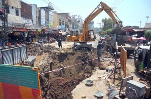 An excavator loads excavated soil onto a tractor trolley during ongoing sewerage and road rehabilitation work on Hussain Agahi Road, with construction activities disrupting traffic in the city’s busy commercial area