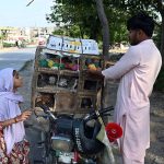 A young girl watches as a vendor sells colourful chicks and live birds from a cage mounted on a motorcycle along a roadside at I-9/4 area in the Federal; Capital