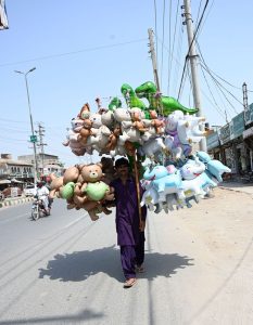 A vendor walks along College Road carrying a large collection of colourful animal-shaped foil balloons for sale, braving the scorching heat to earn his livelihood.