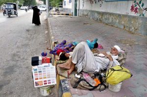 An elderly laborer, waiting for work, rests in the shade on a footpath with his children to escape the scorching heat across the city.