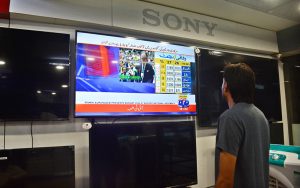 A shopkeeper keeps his eyes fixed on a television screen at his shop while watching Finance Minister Muhammad Aurangzeb present the Federal Budget 2026–27