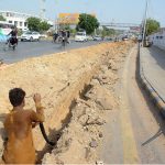 A worker lays a Sui gas pipeline in a deep trench along a busy road near the National Stadium in Karachi, as traffic continues to flow on the adjacent lane