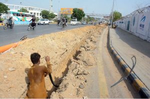 A worker lays a Sui gas pipeline in a deep trench along a busy road near the National Stadium in Karachi, as traffic continues to flow on the adjacent lane