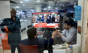 A shopkeeper keeps his eyes fixed on a television screen at his shop while watching Finance Minister Muhammad Aurangzeb present the Federal Budget 2026–27