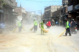 Sanitary workers sweep sand and debris from a road at Doulat Gate after the conclusion of the 10th Muharram (Ashura) procession, as a dust cloud rises during the post-procession cleanliness operation in the city