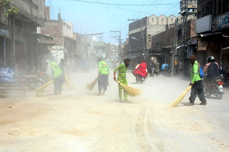 Sanitary workers sweep sand and debris from a road at Doulat Gate after the conclusion of the 10th Muharram (Ashura) procession, as a dust cloud rises during the post-procession cleanliness operation in the city