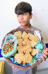 A young street vendor displays snack items for sale while strolling through a neighborhood, seeking customers and earning his livelihood.