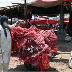 An elderly labourer ties and secures a heavily loaded cart of red mesh packing bags with rope at a busy wholesale vegetable and fruit market