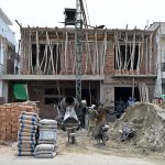 Construction workers busy at a residential building under construction with a cement mixer, concrete hoist, wheelbarrows, bricks and cement bags visible at the active building site