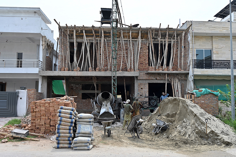 Construction workers busy at a residential building under construction with a cement mixer, concrete hoist, wheelbarrows, bricks and cement bags visible at the active building site