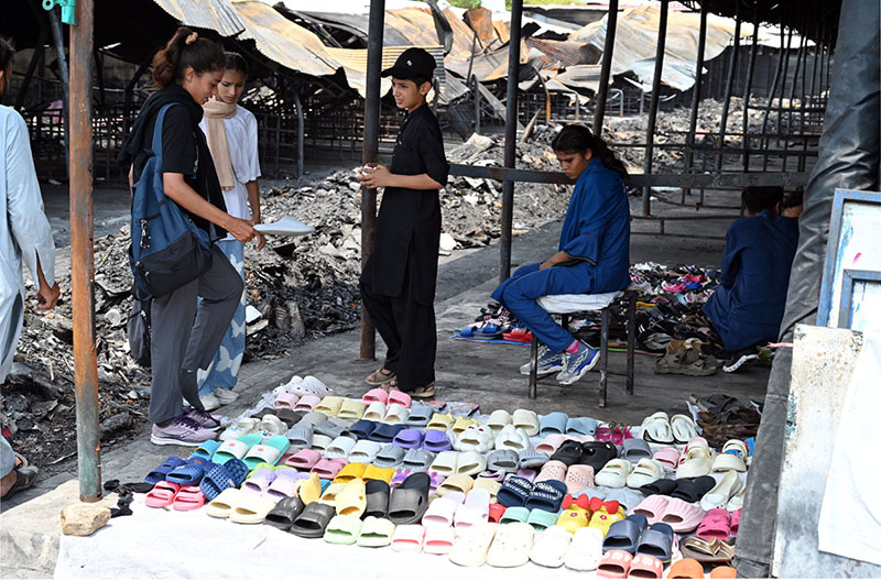 Vendors display footwear for sale amid the burnt ruins of H-9 weekly Bazaar, showing remarkable resilience as they resume trade following the devastating fire that gutted the market