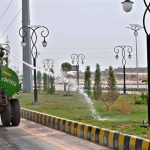 A worker showing water on the plants at center path of road near Chak Shahzad