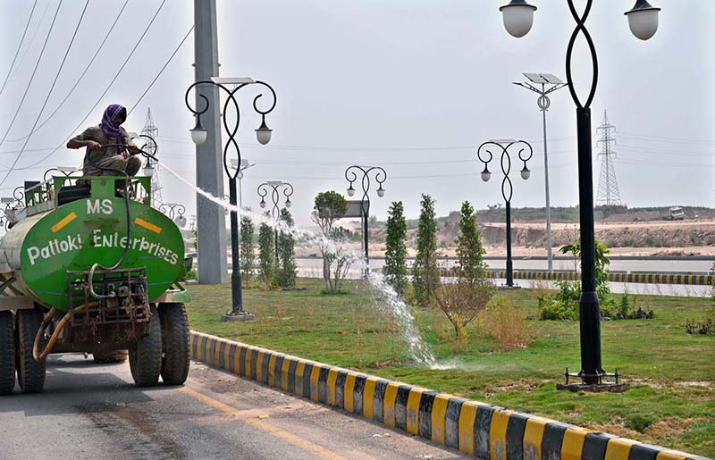 A worker showing water on the plants at center path of road near Chak Shahzad