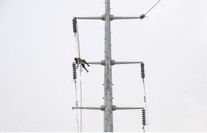 A WAPDA worker installs new power lines on a high electricity pole along Lathrar Road.