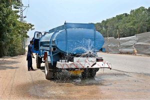 A worker showing water on the plants at center path of road near Chak Shahzad