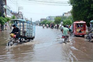 Motorcycles and tricycle rickshaws passing through rain water accumulated on the road after heavy rain in the city.