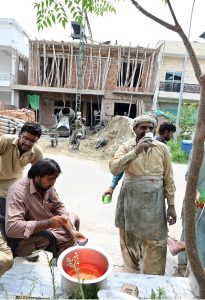 Construction workers busy at a residential building under construction with a cement mixer, concrete hoist, wheelbarrows, bricks and cement bags visible at the active building site