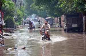 Motorcycles and tricycle rickshaws passing through rain water accumulated on the road after heavy rain in the city.