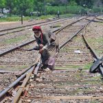 An elderly railway worker is manually operating a track switch at the railway yard to guide trains onto the designated rail line in the city