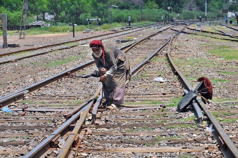 An elderly railway worker is manually operating a track switch at the railway yard to guide trains onto the designated rail line in the city