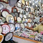 A vendor arranging and displaying wall clocks to attract the customers at weekly bazaar, Peshawar Morr