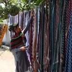 A young vendor displays and sells cotton handkerchiefs by the roadside during the severe summer heat
